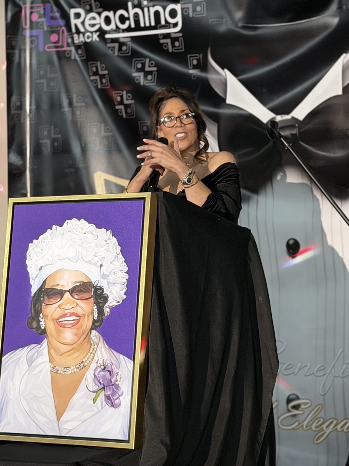 Leah Douglas Wooten speaking at a Reaching Back event beside a framed portrait